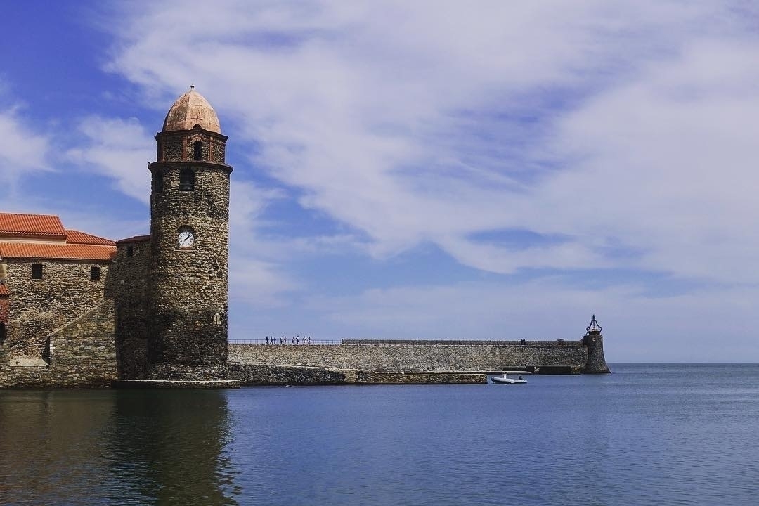 Auto-generated description: A historic coastal building with a prominent clock tower stands beside a calm sea under a partly cloudy sky.