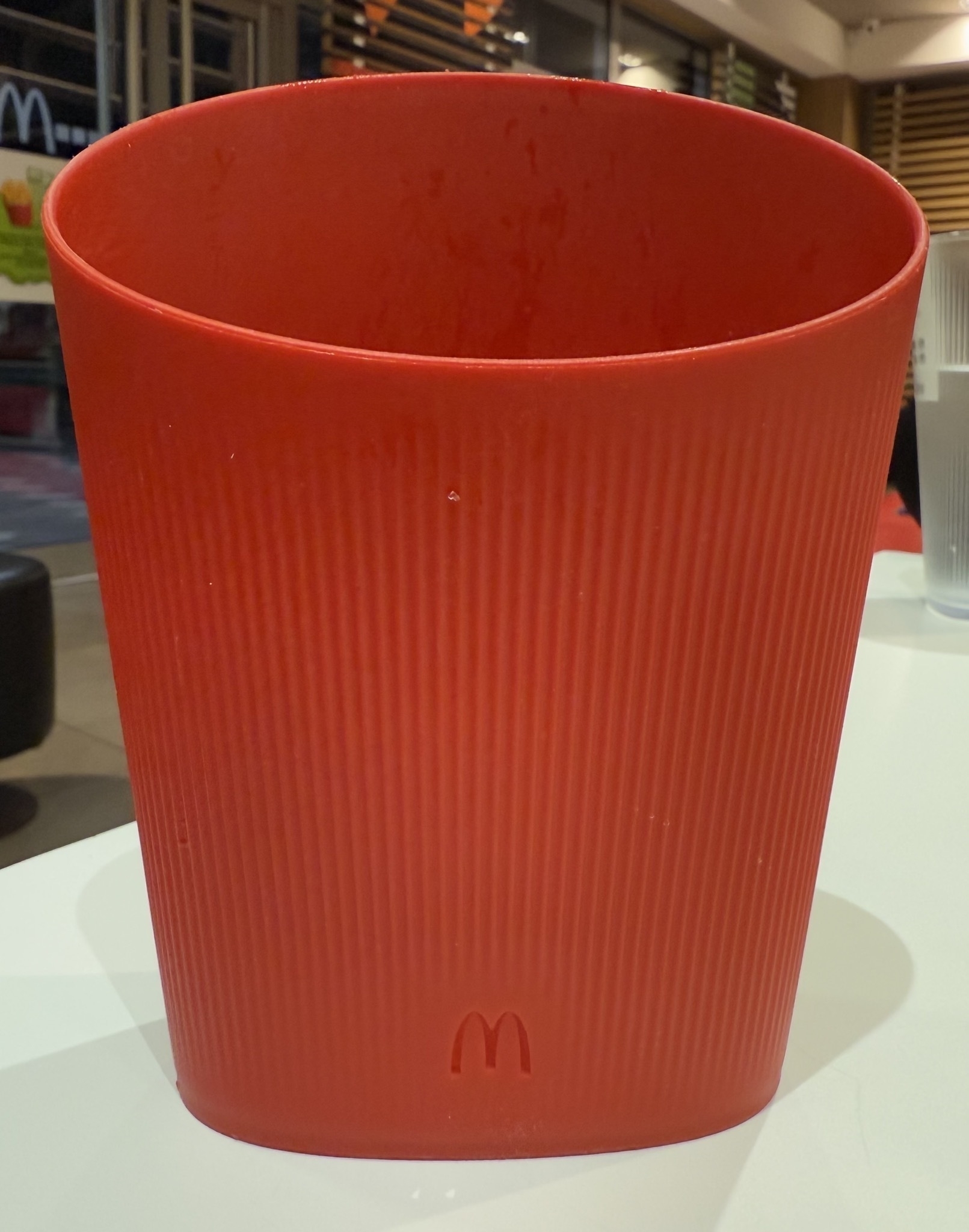 A red, ribbed container with a logo resembling McDonald’s is placed on a white surface.