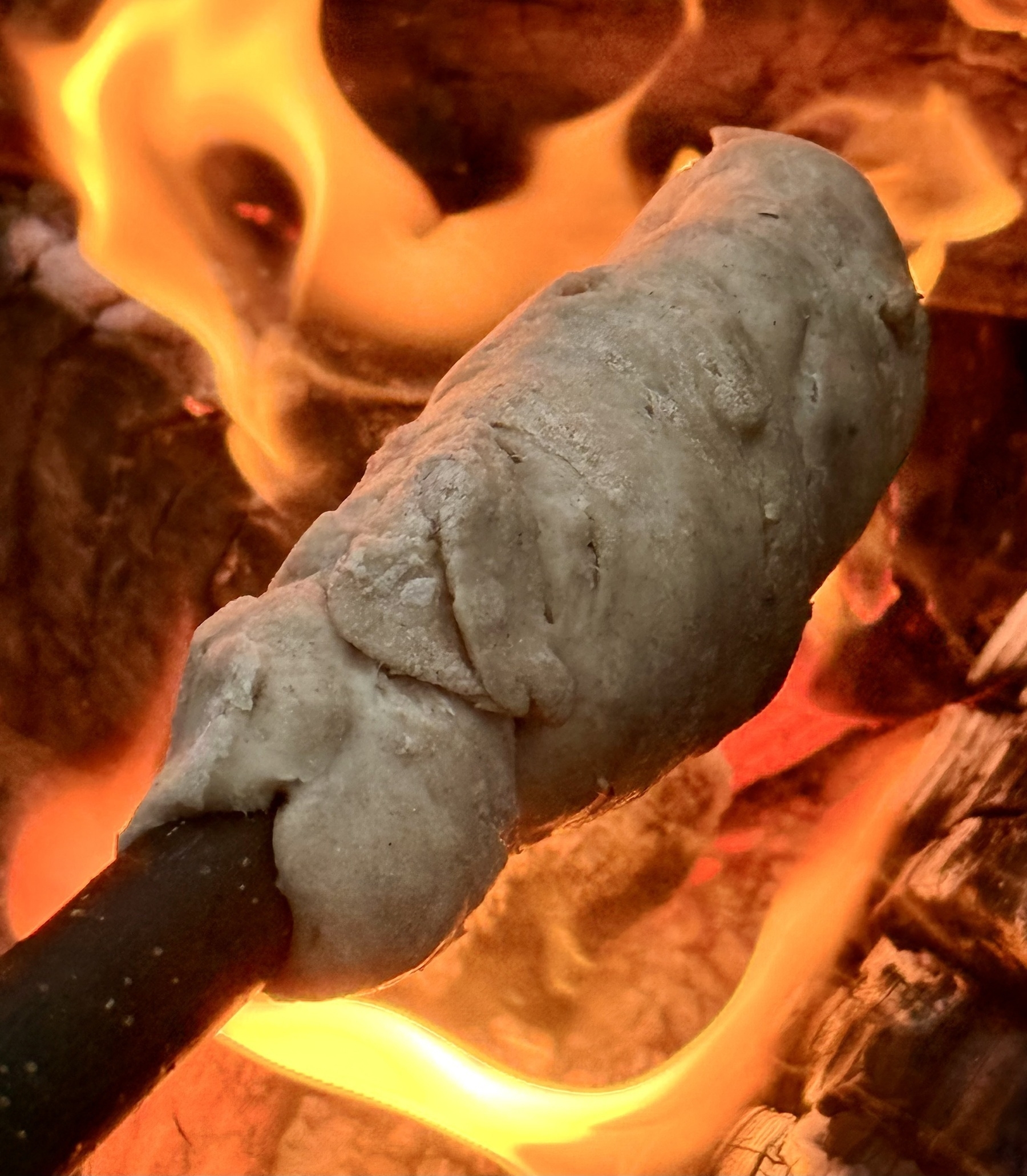 Bread dough wrapped around a stick is being roasted over an open flame.